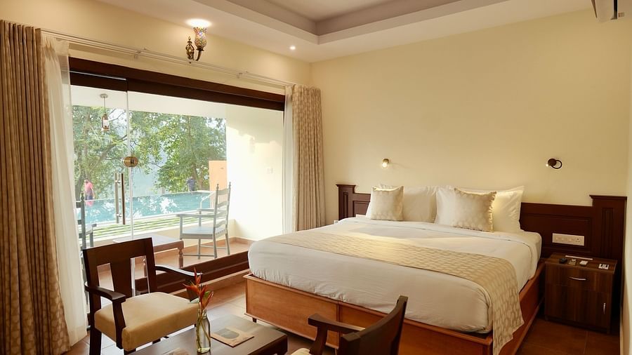 An image of a  Lake view family cottage with private pool featuring a bedroom, a bedside, two chairs and a centre table, and a balcony - Fragnant Nature Kollam