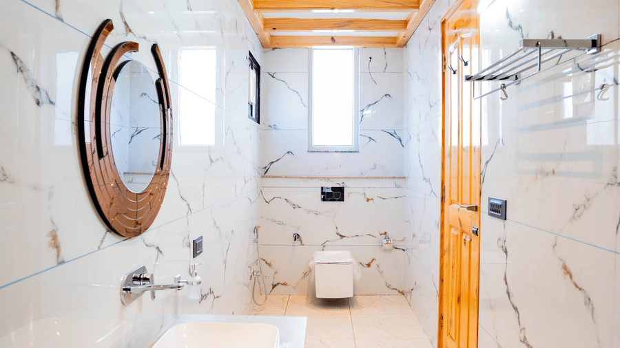 A modern, long-profile bathroom with marble walls, a round mirror, and a wood-slat ceiling - Golden Oak By The Lake Hill, Khurpatal