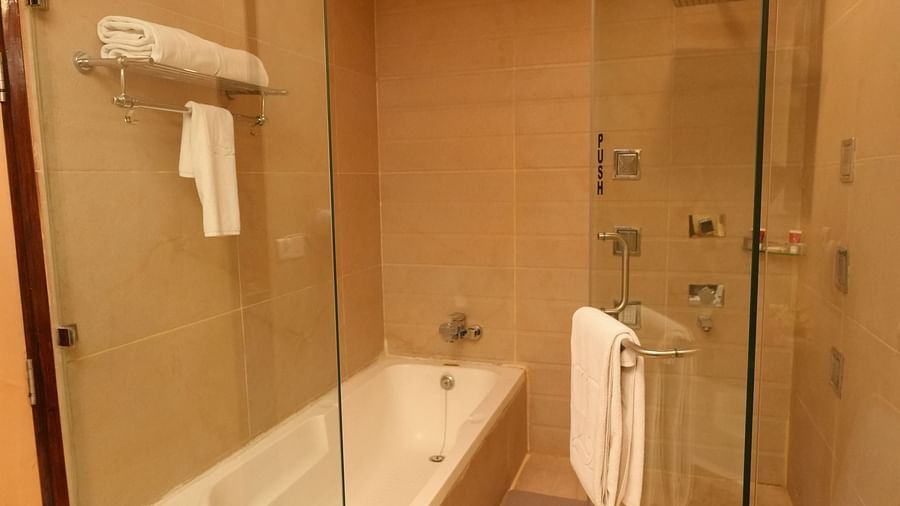 Modern bathroom with a glass-enclosed shower, bathtub, and white towels - Grand Plaza Lords Inn Jammu