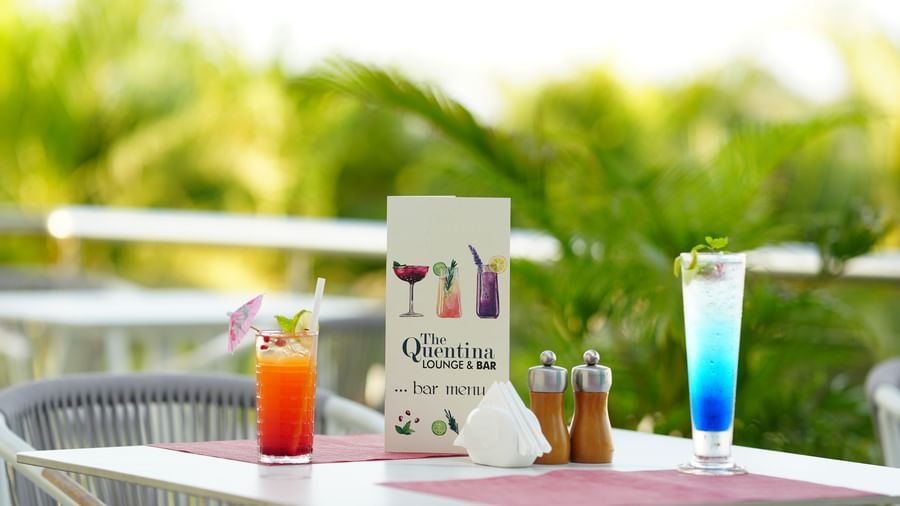Outdoor dining table with drinks, a menu card and condiments placed neatly at Grande Bay Resort & Spa.