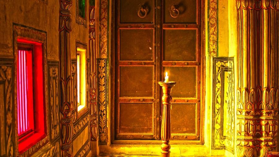 A richly decorated hallway at Fort Barli, illuminated with warm light, leads towards a grand wooden door.