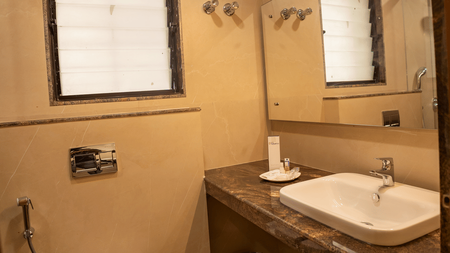 Bathroom area showing the toilet bowl, hand spray, frosted window, countertop washbasin, and vanity mirror at Hotel Grand Sabarees Madurai.
