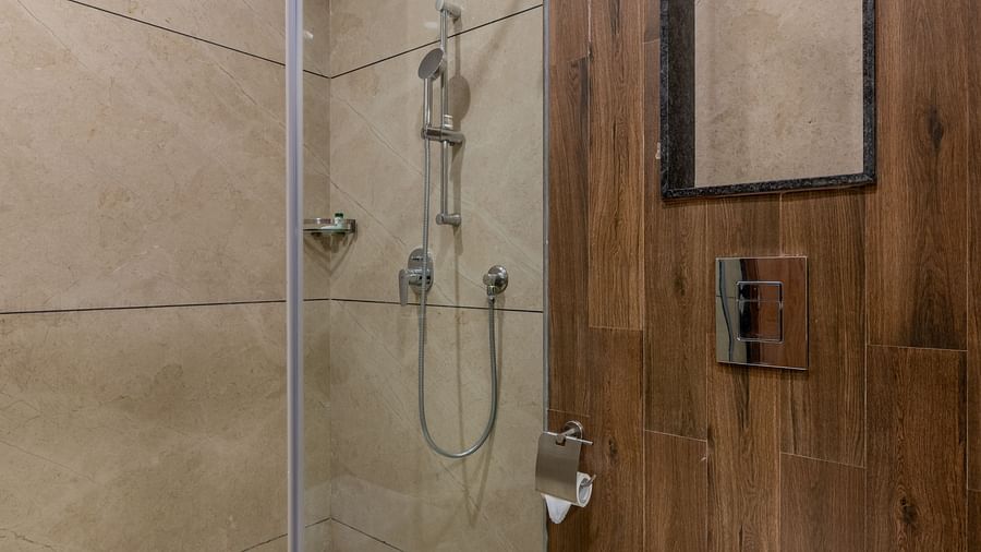A close-up view of a shower area at Hotel Highway King, Bagru, with light-colored tiles and a modern showerhead.