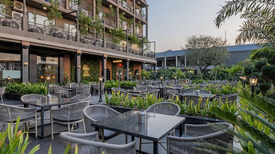 Outdoor seating area at Hotel Highway King, Bagru, with tables and chairs surrounded by plants and hotel balconies.