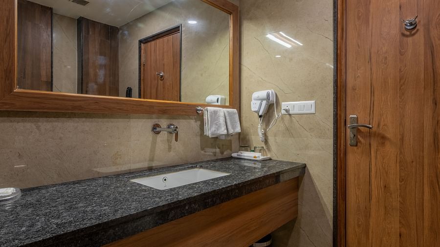 A modern bathroom at Hotel Highway King, Bagru, with a vanity, sink, mirror, and toilet. The door appears to be made of wood.