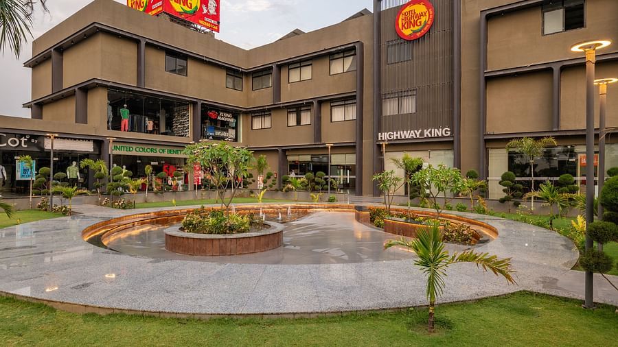 Facade and well-manicured lawn of Hotel Highway King, Behror, which also features a large illuminated logo of the property.