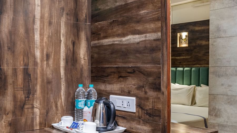 A section of the wooden shelves on with a mirror and a tray on which tea and coffee making sachets have been placed alongside water bottles in the Maharaja Deluxe Room of Hotel Highway King, Behror.