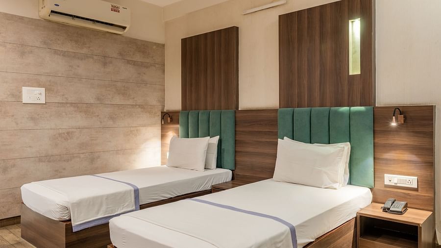 Twin beds with upholstered headboards and bedside tables in the Maharaja Deluxe Rooms of Hotel Highway King, Behror.