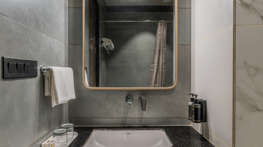 Bathroom with a washbasin, mirror, wooden vanity, and tiled walls.