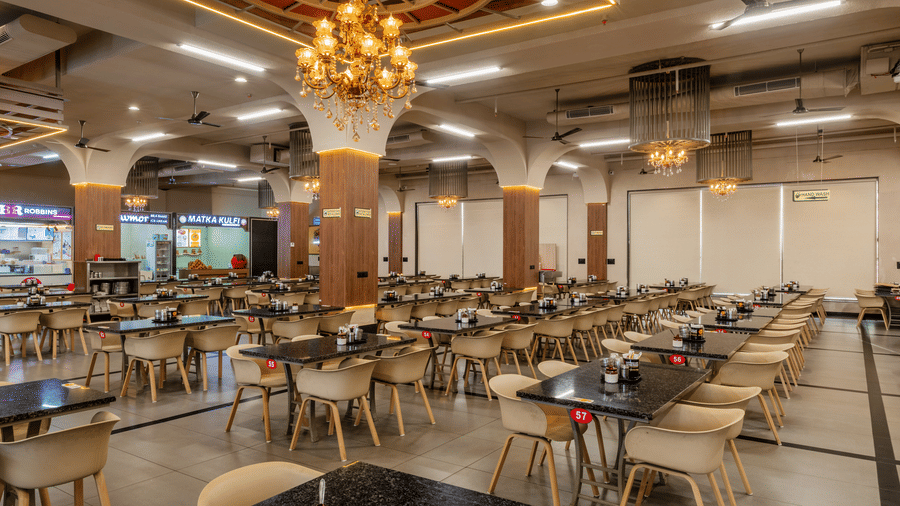 Spacious dining hall with long tables, multiple chairs, and a large central chandelier hanging from the ceiling at Hotel Highway King, Harmada.