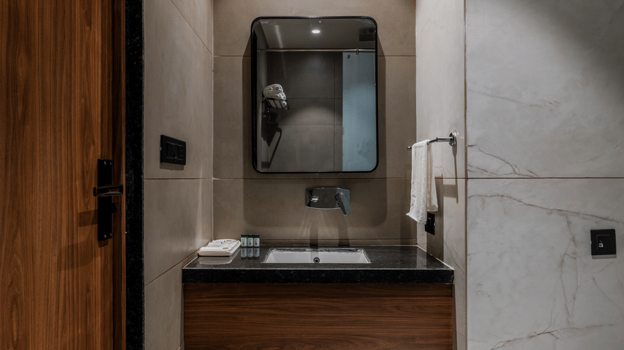 A washbasin, a mirror, and a wooden door near the toilet at Hotel Highway King, Harmada.
