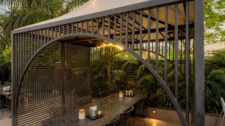 A small gazebo-like wooden seating structure with a curved roof surrounded by greenery at Hotel Highway King, Jaipur.