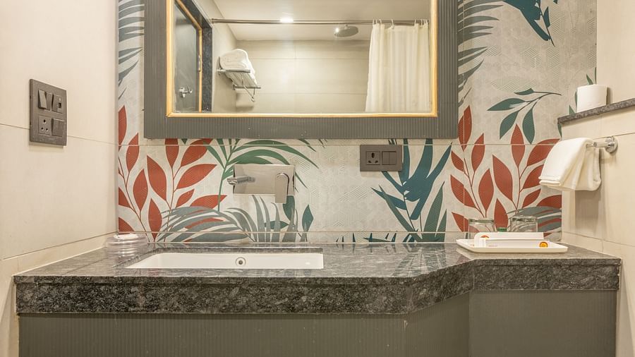 A toilet and washbasin with mirror in a tiled flowery bathroom at Hotel Highway King, Jaipur.