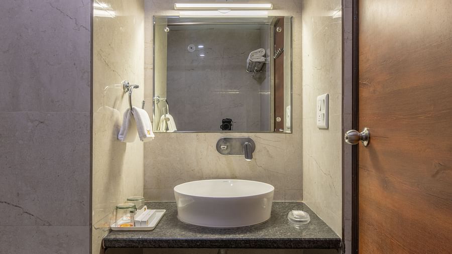 A narrow bathroom with washbasin, mirror, and wooden door at Hotel Highway King, Jaipur.