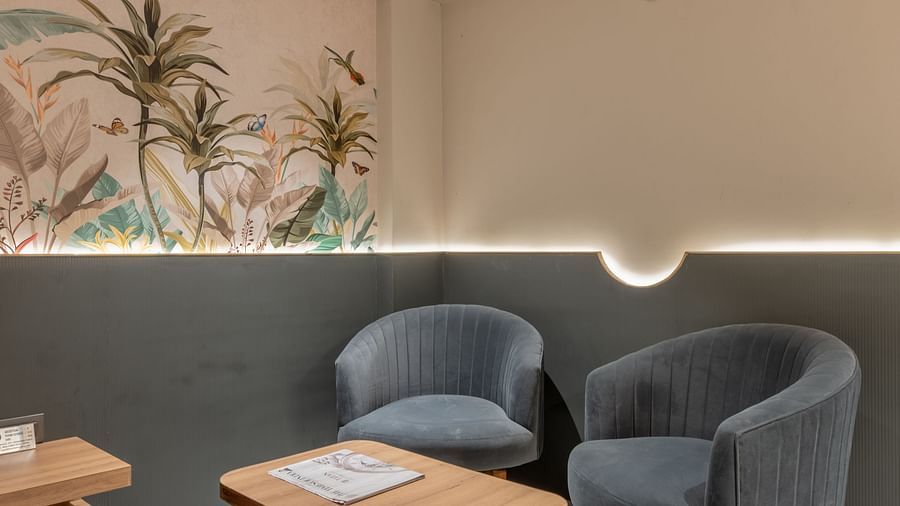 A seating area with two grey chairs and wooden table beside a wall mural at Hotel Highway King, Jaipur.