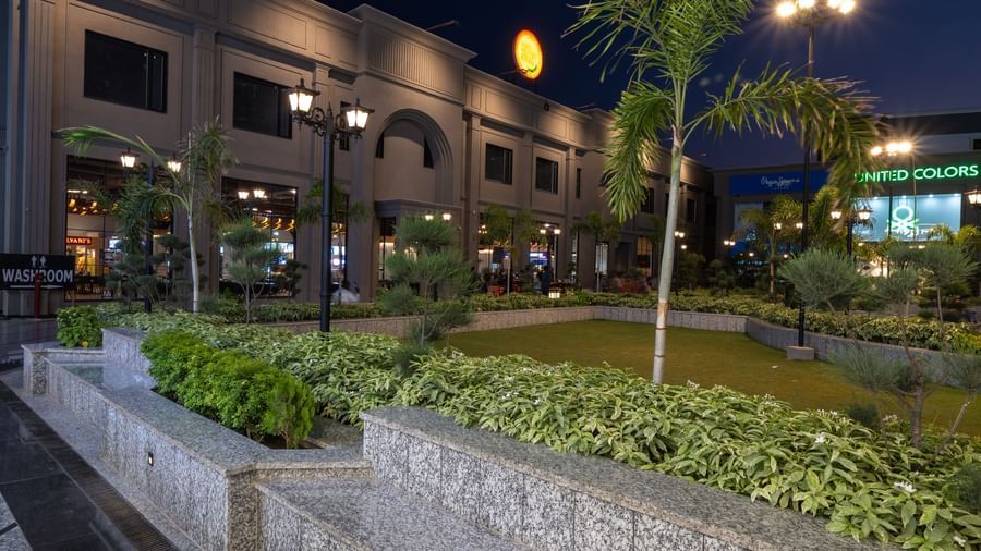 Walkway and landscaped garden with palm tree at Hotel Highway King, Kishangarh lit up at night.