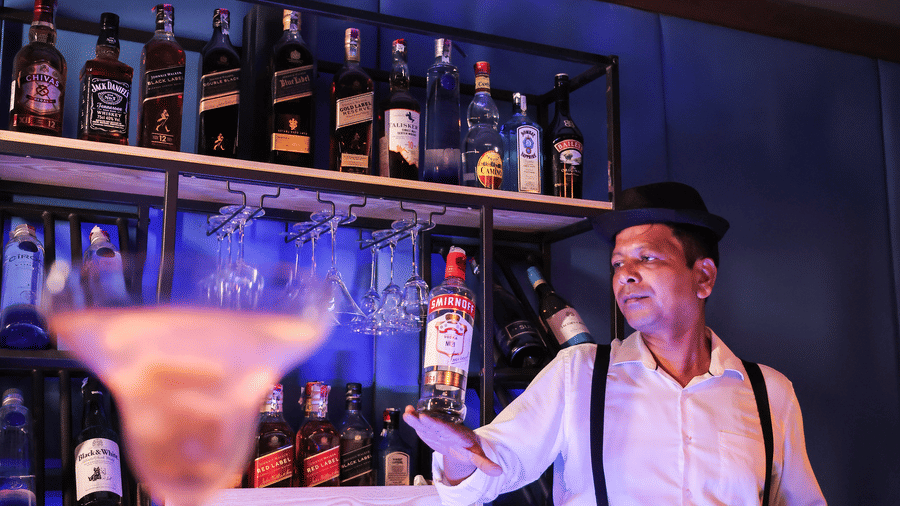 A bartender standing behind a bar with rows of bottles, illuminated by strong blue and purple nightclub lighting at Hotel Hukam's Lalit Mahal.