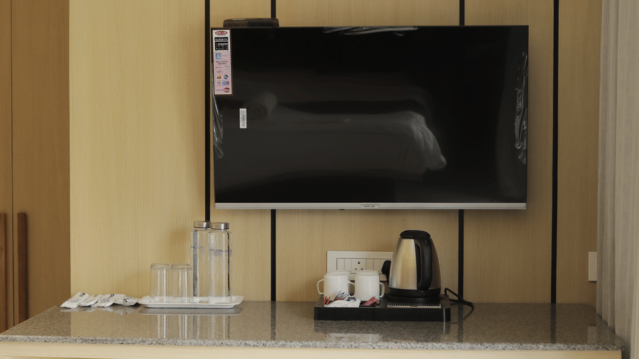 Room desk and entertainment center area featuring a mounted flat-screen television above a counter with a kettle and cups at Hotel Seagull Digha
