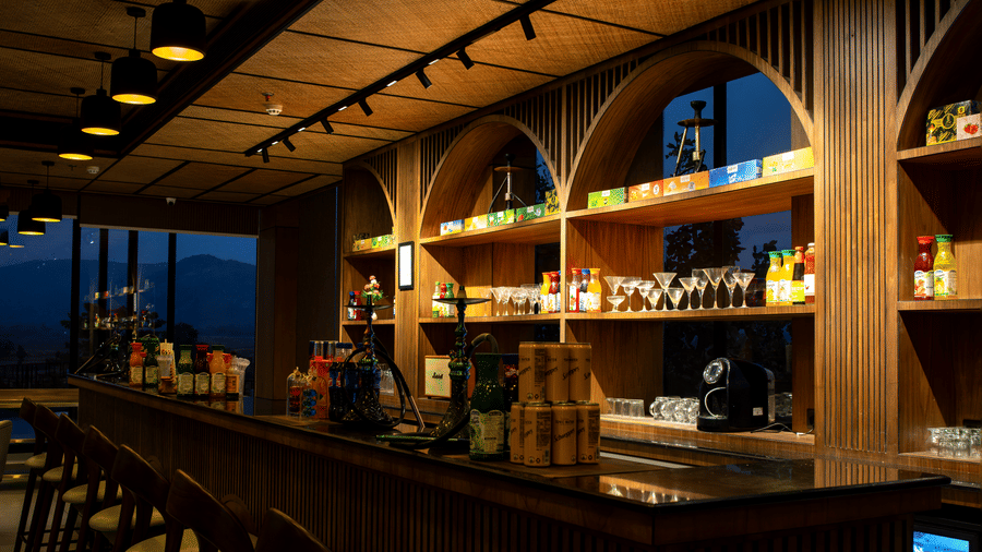 A bar area featuring a wooden counter, high stools, and arched shelving at Hotel Sonar Bangla, Ajodhya Hills.