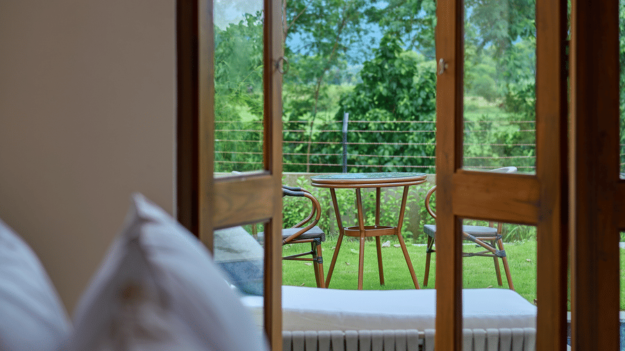 An indoor view over bed pillows featuring open doors leading to an outdoor patio with seating at Hotel Sonar Bangla, Ajodhya Hills.