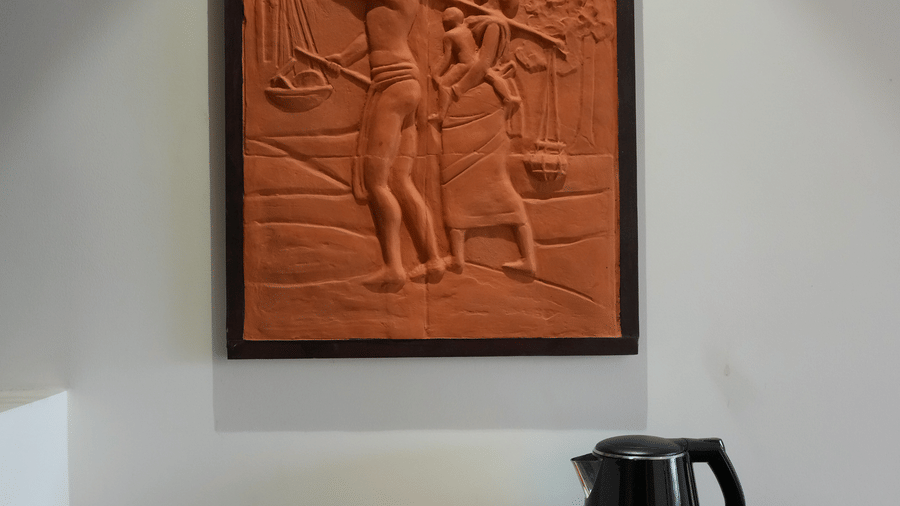 A room detail featuring a black counter with a kettle on a tray and a square terracotta wall artwork at Hotel Sonar Bangla, Ajodhya Hills.
