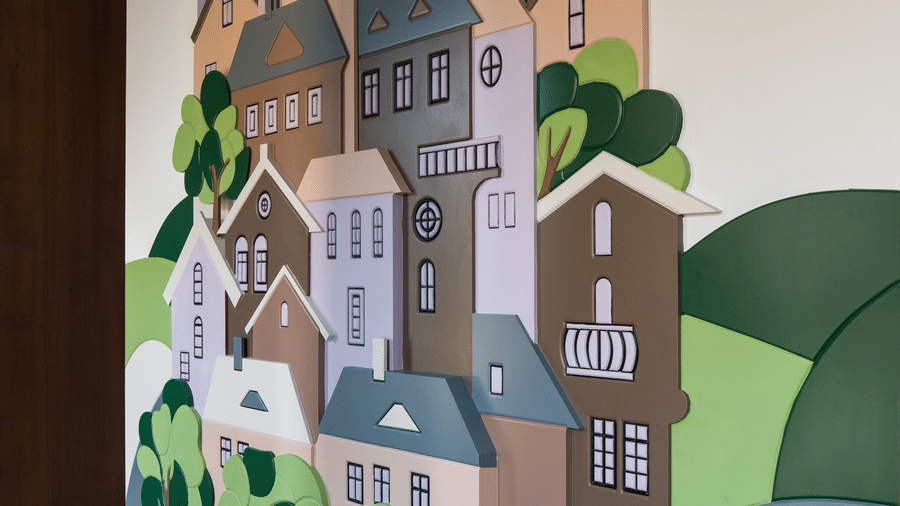 An indoor wall featuring a colourful painted mural of a town with buildings and trees above a checkered floor at Hotel Sonar Bangla, Ajodhya Hills.