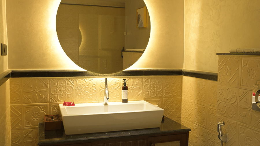 A bathroom vanity with a white rectangular sink and a large illuminated circular mirror at Hotel Sonar Bangla, Mayapur.