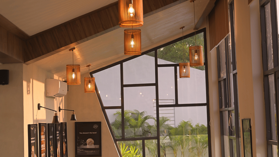 A warm corner of the cafe featuring comfortable seating, pendant lights, and large glass windows at Hotel Sonar Bangla, Mayapur.