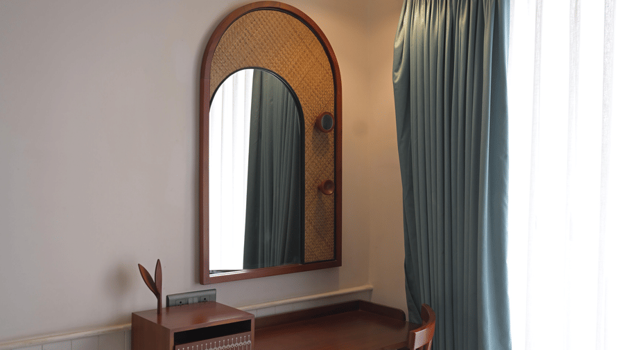 A dark wood dressing table with a matching chair and mirror next to blue curtains at Hotel Sonar Bangla, Mayapur.