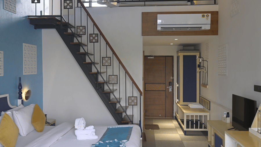 A view of a guest room showing a bed on the lower level and a staircase leading to a mezzanine balcony at Hotel Sonar Bangla, Mayapur.