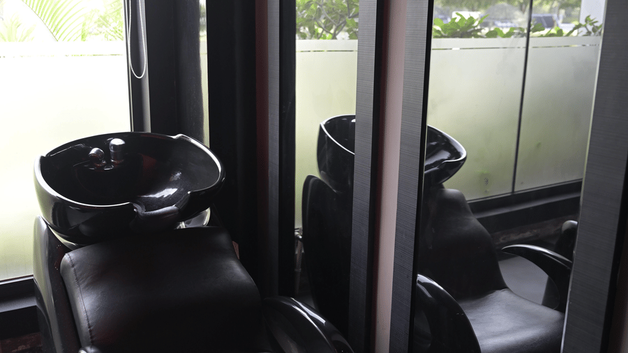 A salon station with a black styling chair placed beside large windows at Hotel Sonar Bangla, Mayapur.