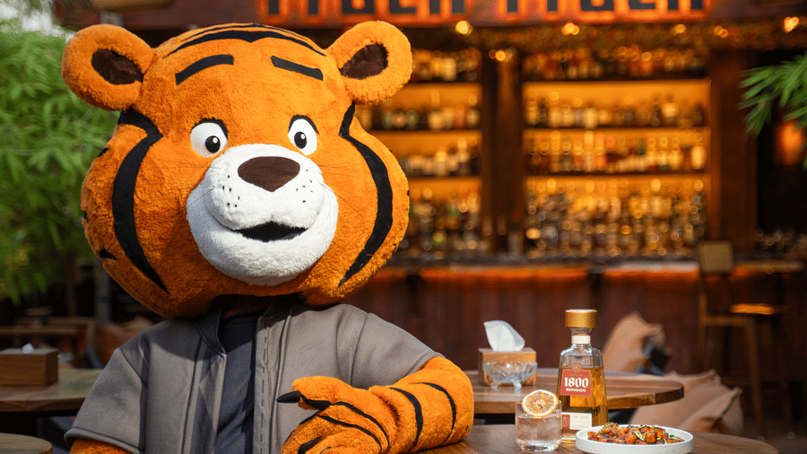 A person in a tiger mascot costume standing near a dining table at Infiniti Hotel, Indore.