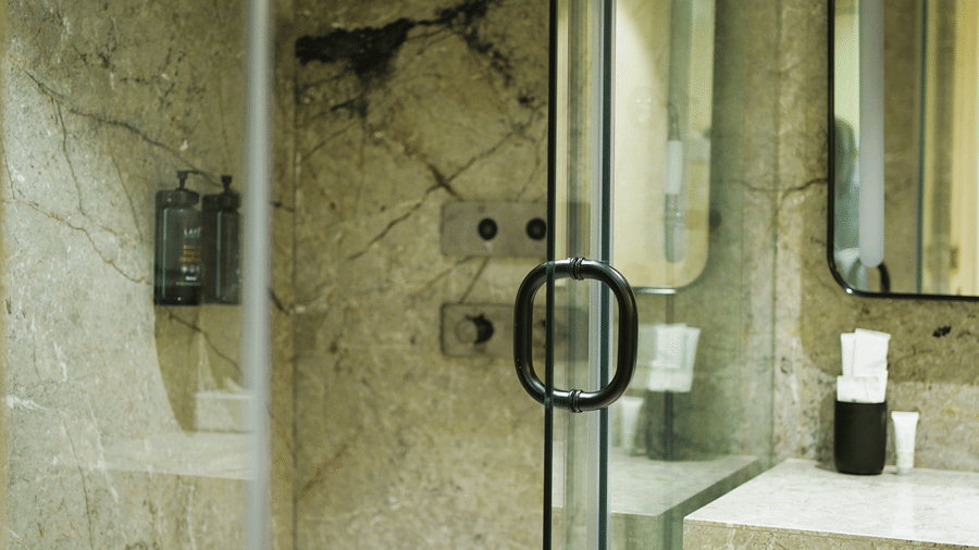 A bathroom at Infiniti Hotel, Indore featuring glass shower enclosure, overhead shower, marble wall, and vanity unit.