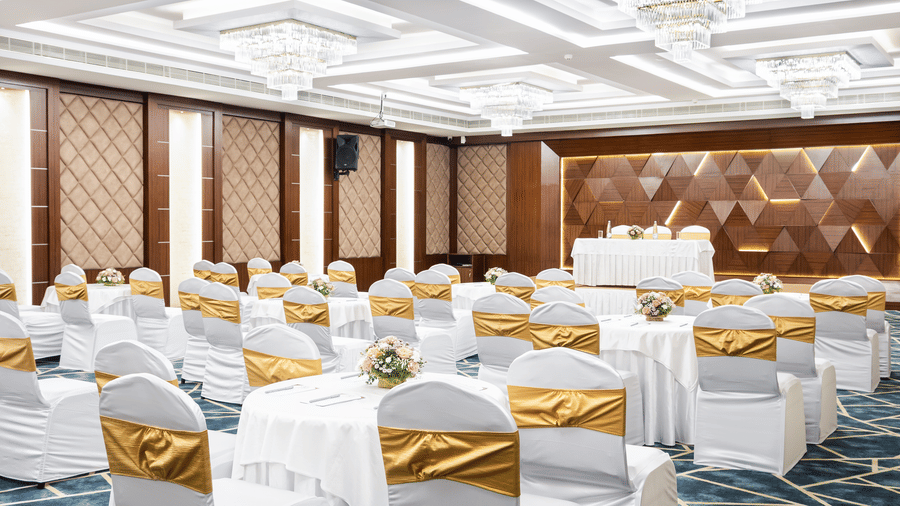 A hall at Jenneys Residency with chairs, chandeliers, and checkered floor.