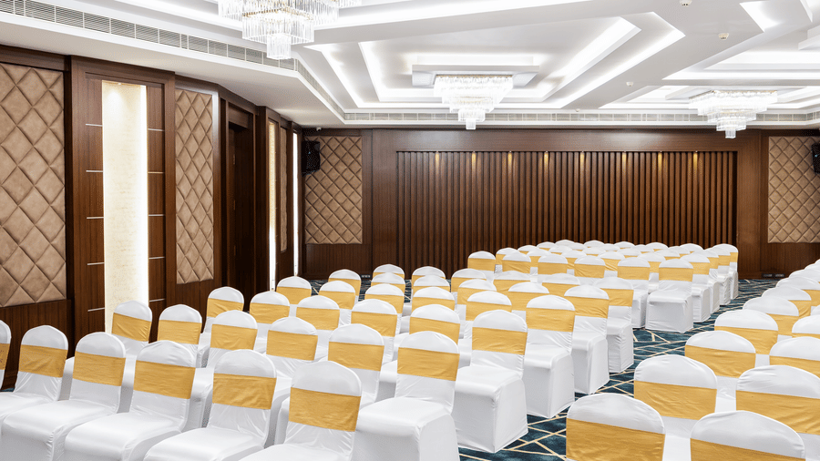 A hall at Jenneys Residency with chairs, chandeliers, and checkered floor.