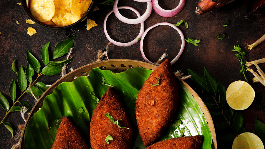 Traditional golden-brown fried snacks served on a banana leaf with onion rings and herbs - Jenneys Residency, Coimbatore