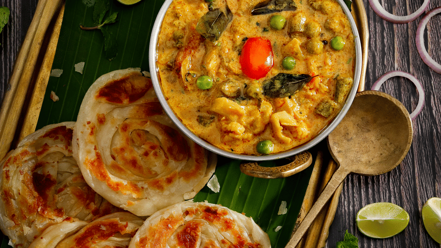 A traditional South Indian meal featuring flaky malabar parottas served with a side of vegetable curry on a banana leaf - Jenneys Residency, Coimbatore