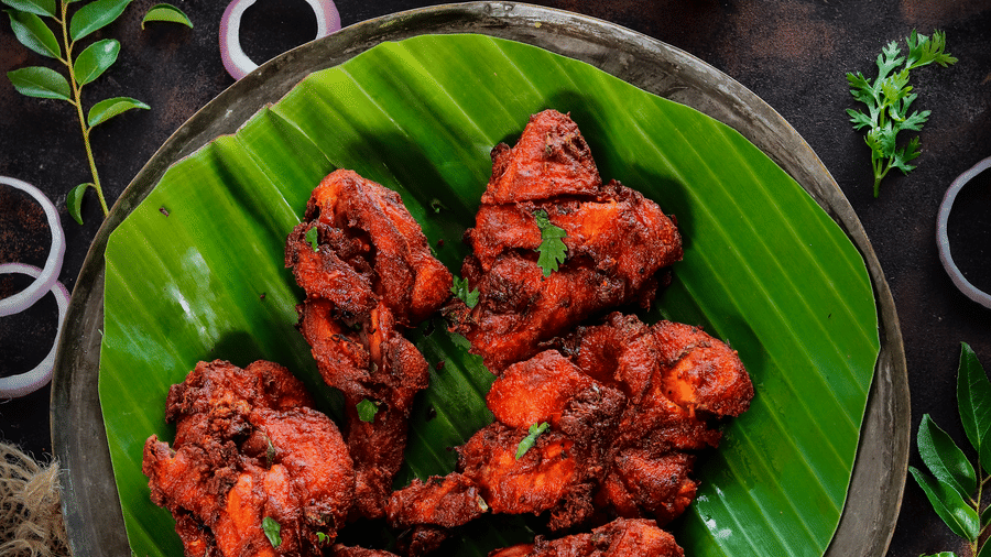 A top-down shot of spicy red tandoori chicken pieces served on a banana leaf with lemon - Jenneys Residency, Coimbatore
