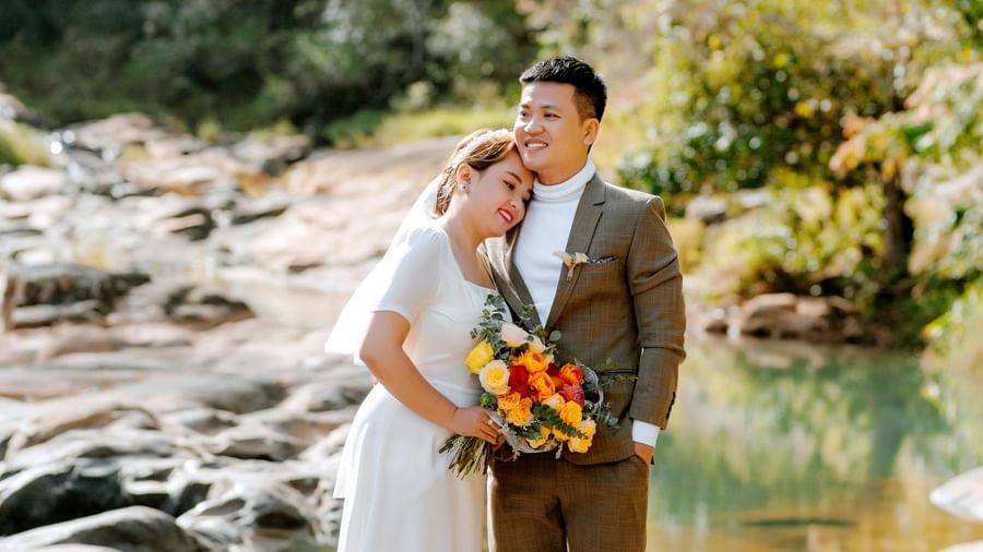 A bride and groom stand by a flowing river in a natural, outdoor setting, looking at each other