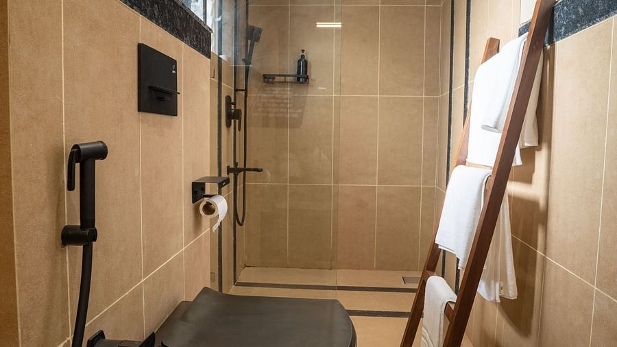 Compact bathroom featuring black sanitary ware, glass shower area, and wooden ladder towel rack at Kssemya.
