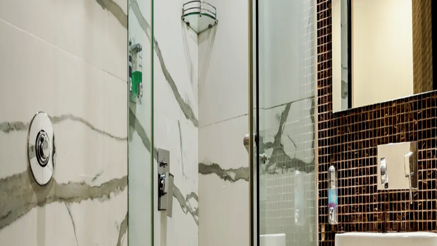 Bathroom at Kumar Resort by Turtle with a glass-enclosed rain shower, marble walls, vessel sink on a stone counter and wall-hung toilet.
