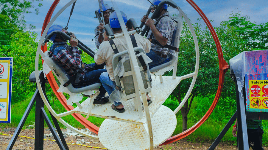 A circular thrill ride with suspended seats enclosed in a metal frame, set against a clear blue sky.