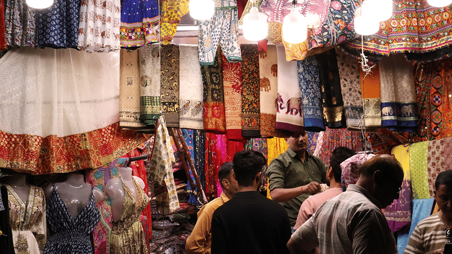 A night bazaar clothing stall lit by hanging bulbs, with colourful garments on display