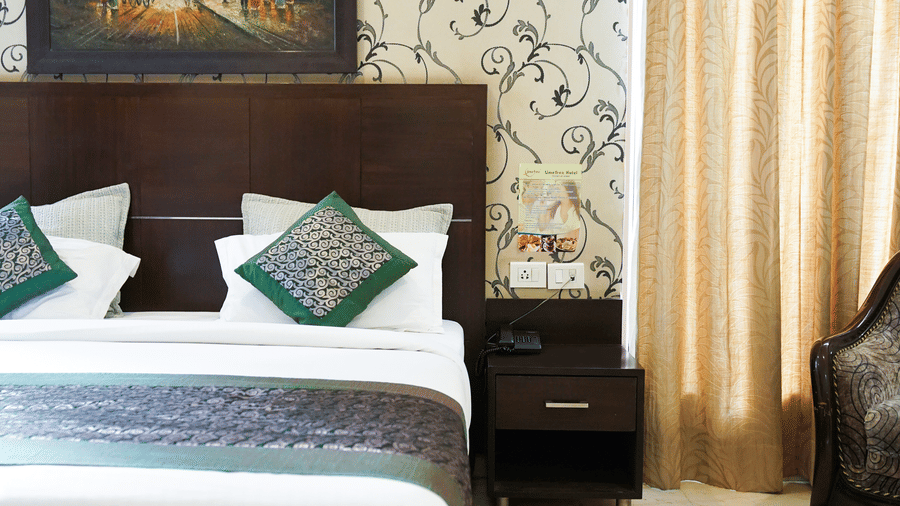 Guest room with a dark wood headboard, a framed Parisian painting, damask wallpaper, gold curtains, and a carved armchair.