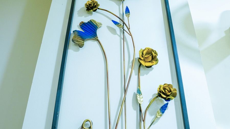 Metal wall art at Lime Tree Hotel Near 32nd Avenue with blue and gold flowers set in a black rectangular frame mounted on a white wall.