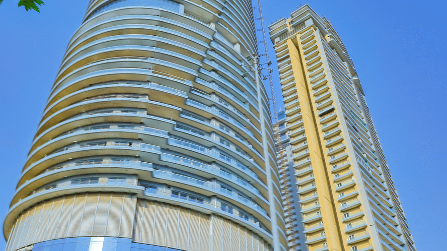 Exterior view of Livbox Supernova, Noida under a bright blue sky with branches of a tree in the corner.