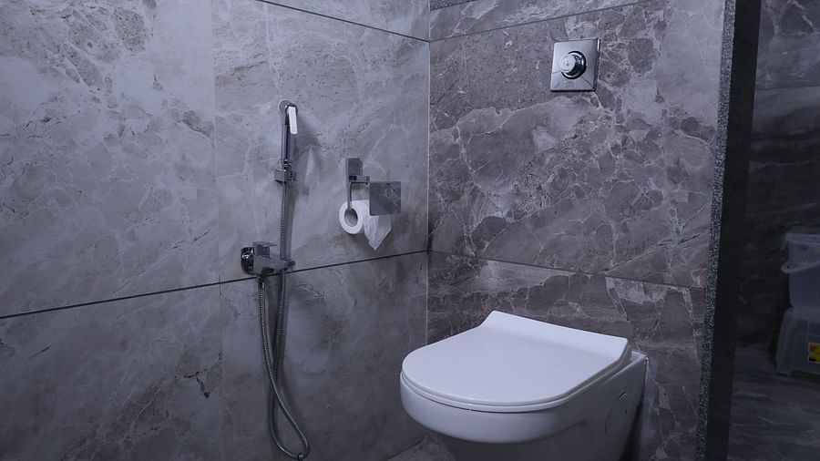 A compact bathroom features a toilet, a shower hose on the wall, and a towel rack above the toilet - Lords Eco Inn Navsari.