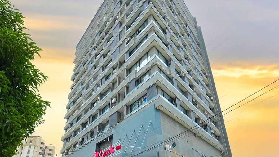 A uniquely designed triangular building with a modern facade, photographed at sunset with trees and street visible.