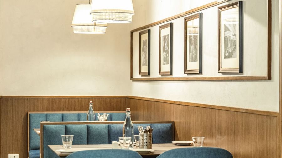 A dining area at Mango Hill Central, Chennai, with blue upholstered chairs and booths. A wooden wall panel is on the left.