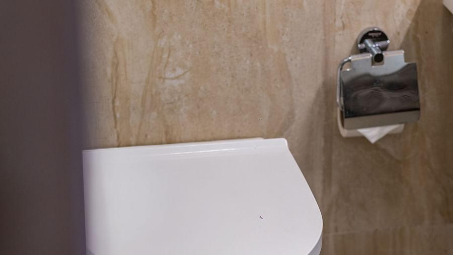 A modern white wall-mounted toilet with a closed lid, against a backdrop of beige and brown patterned tiles - Mango Hill Resort, Coimbatore